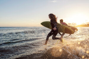 couple running into water at sunset with surfboards