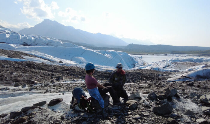 person puts crampons onto another person on an Alaska glacier