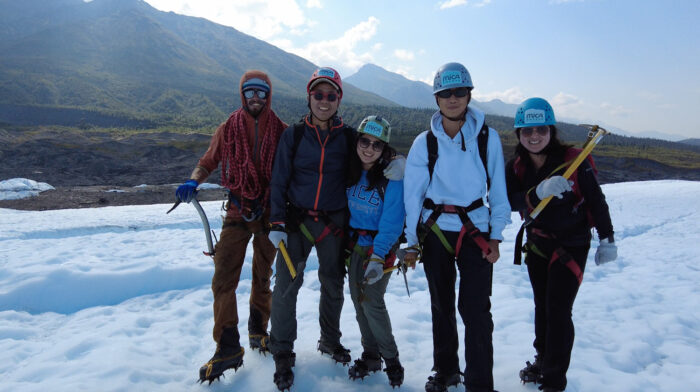 family and glacier guide smile with helmets on