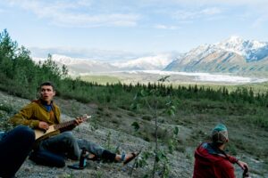 man plays guitar in front of mountains