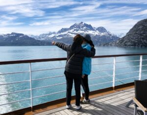 two people point at snowy mountains from a boat deck