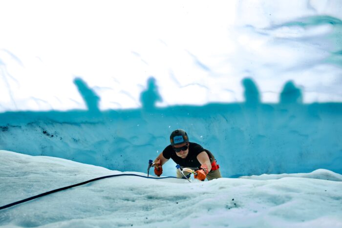 Ice climber focuses while swinging tools into blue ice wall