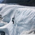 person climbing up glacier ice on bluebird day in Alaska