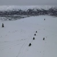 aerial shot of snowmobilers headed to overcast mountains