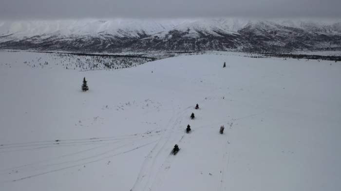 aerial shot of snowmobilers headed to overcast mountains