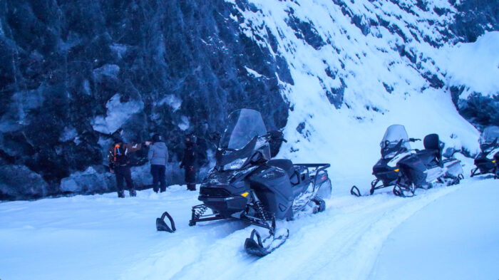 white snow on ice wall with three people and snowmobiles