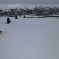 A line of snowmobiles heads into a cloudy mountain range