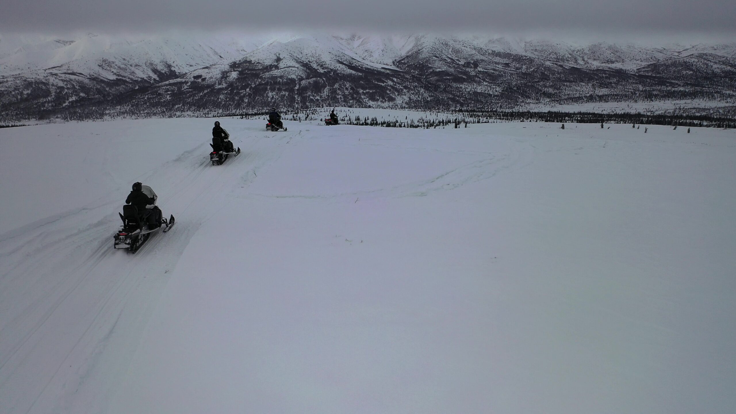 A line of snowmobiles heads into a cloudy mountain range