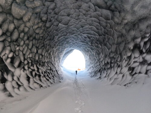 person walking out of ice cave towards red helicopter