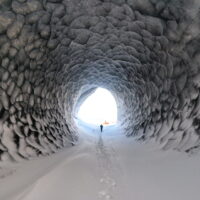 person walking out of ice cave towards red helicopter